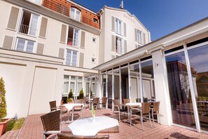 A hotel with a covered outdoor patio featuring wicker furniture and a glass-enclosed dining area.
