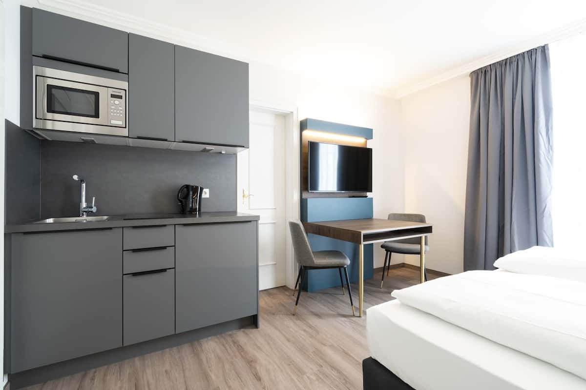 Ein modernes Hotelzimmer mit einer Küchenzeile, einem Flachbildfernseher, einem Bett und einem Schreibtisch.