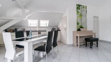 Een moderne keuken met witte kasten, een eethoek met een witte tafel en zwarte stoelen, en een piano in de hoek.