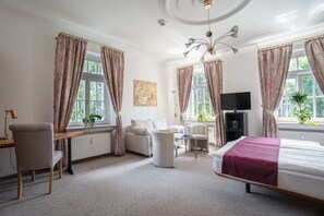 A hotel room with a bed, a sofa, a desk with a lamp, a TV, and a radiator. - Aparthotel Villa Freisleben (Dresden)