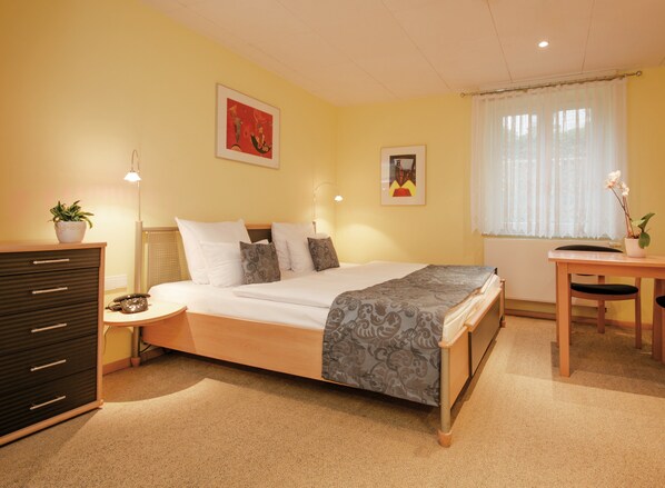 A neatly arranged bedroom with a bed, bedside table, lamp, dresser, and a window with curtains. - Aparthotel Villa Freisleben (Dresden)