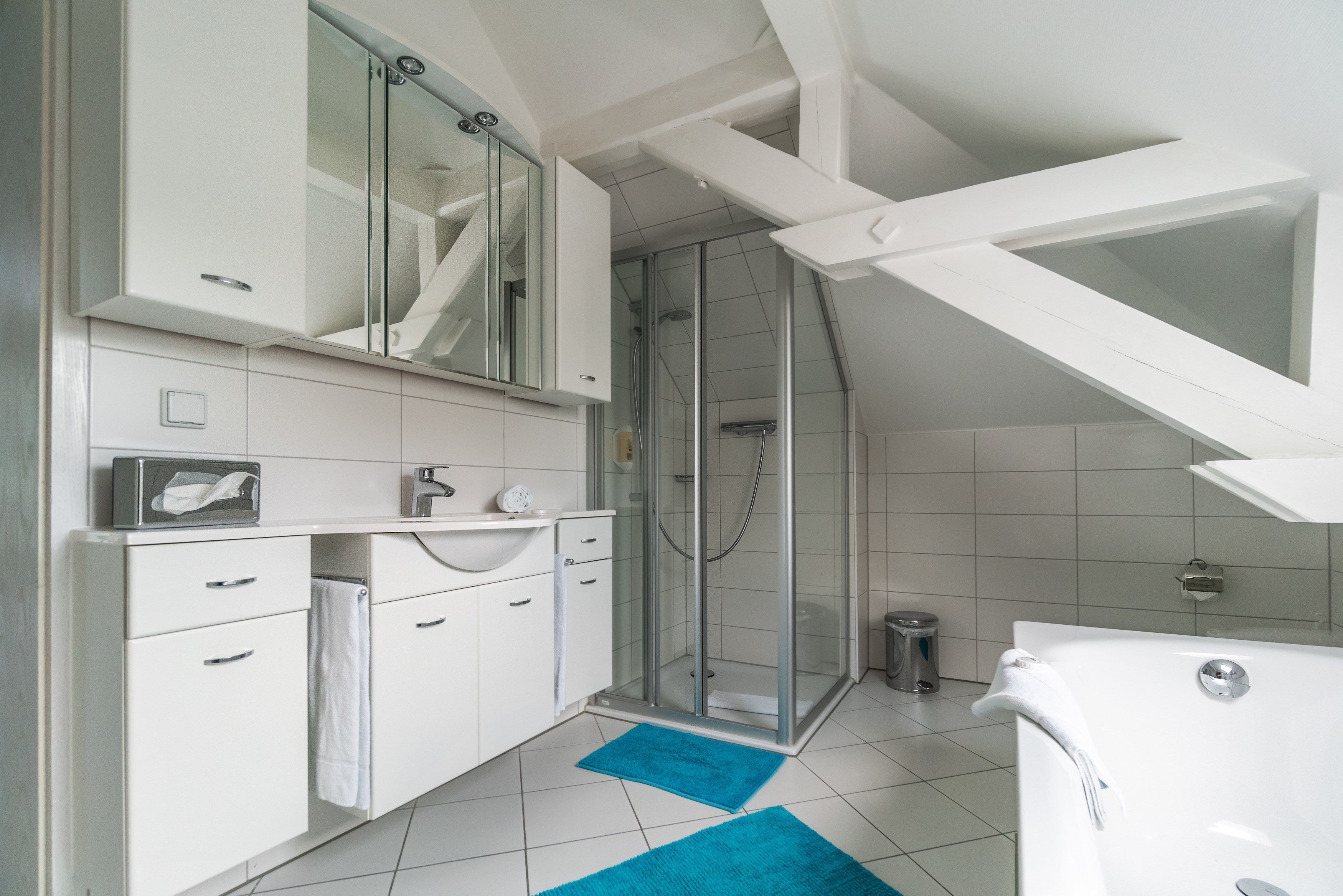 Un baño moderno con ducha, muebles blancos y una alfombra de baño azul.