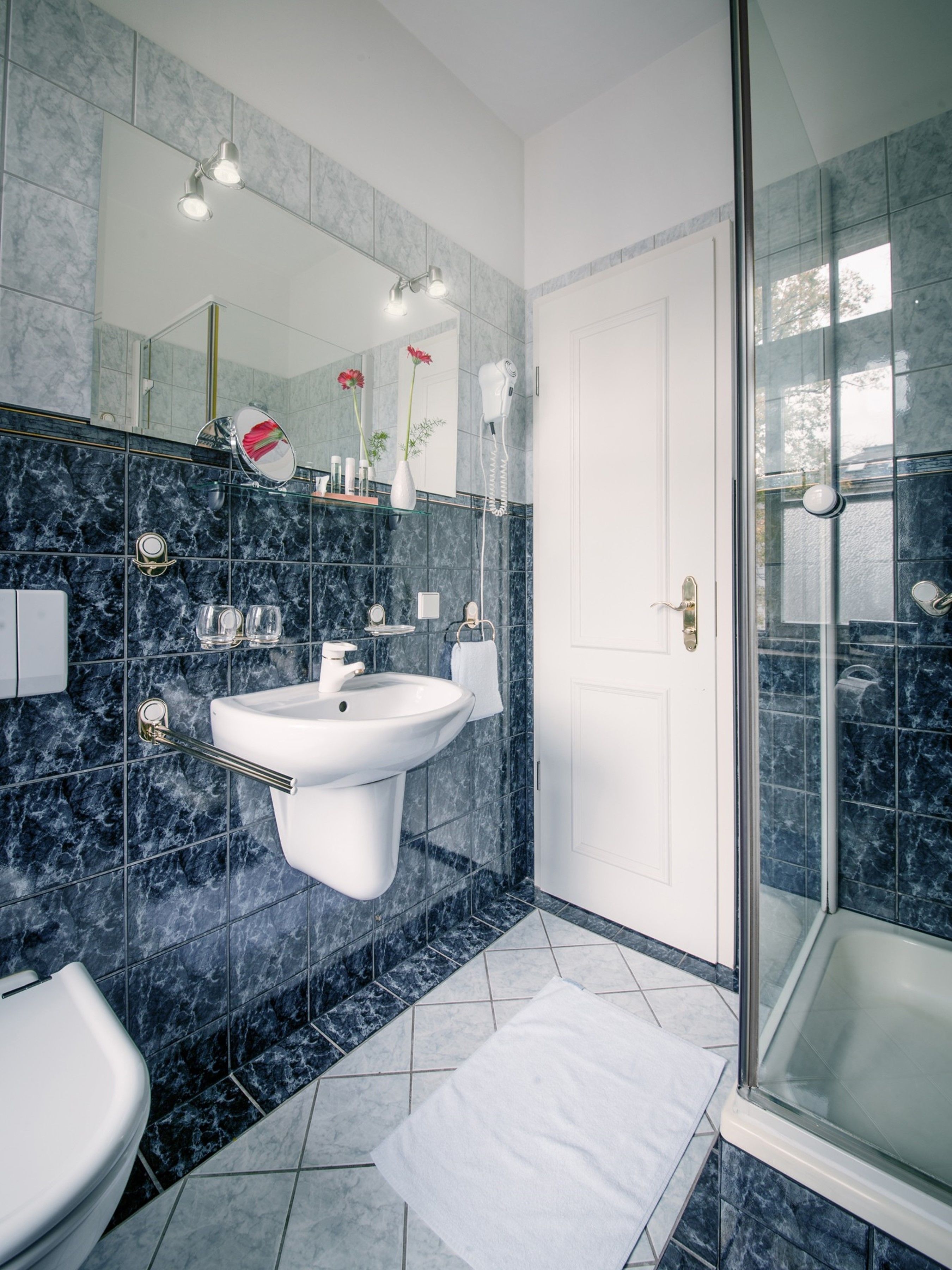 Un baño moderno con un lavamanos blanco, cabina de ducha con mampara de vidrio y pared revestida de mármol.