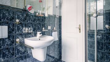 Un baño moderno con un lavamanos blanco, cabina de ducha con mampara de vidrio y pared revestida de mármol.