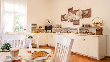 Une table dressée pour le petit-déjeuner, avec une machine à café, des fruits, des viennoiseries et un croissant.