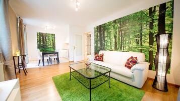 A modern living room with a glass coffee table, a white sofa, and a large forest-themed wall mural.