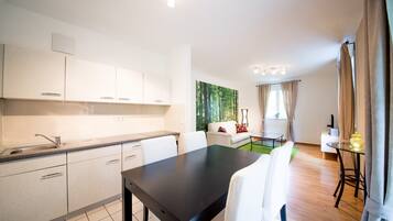 A modern kitchen with white cabinets, a black dining table, and a living area with a sofa and a green wall.