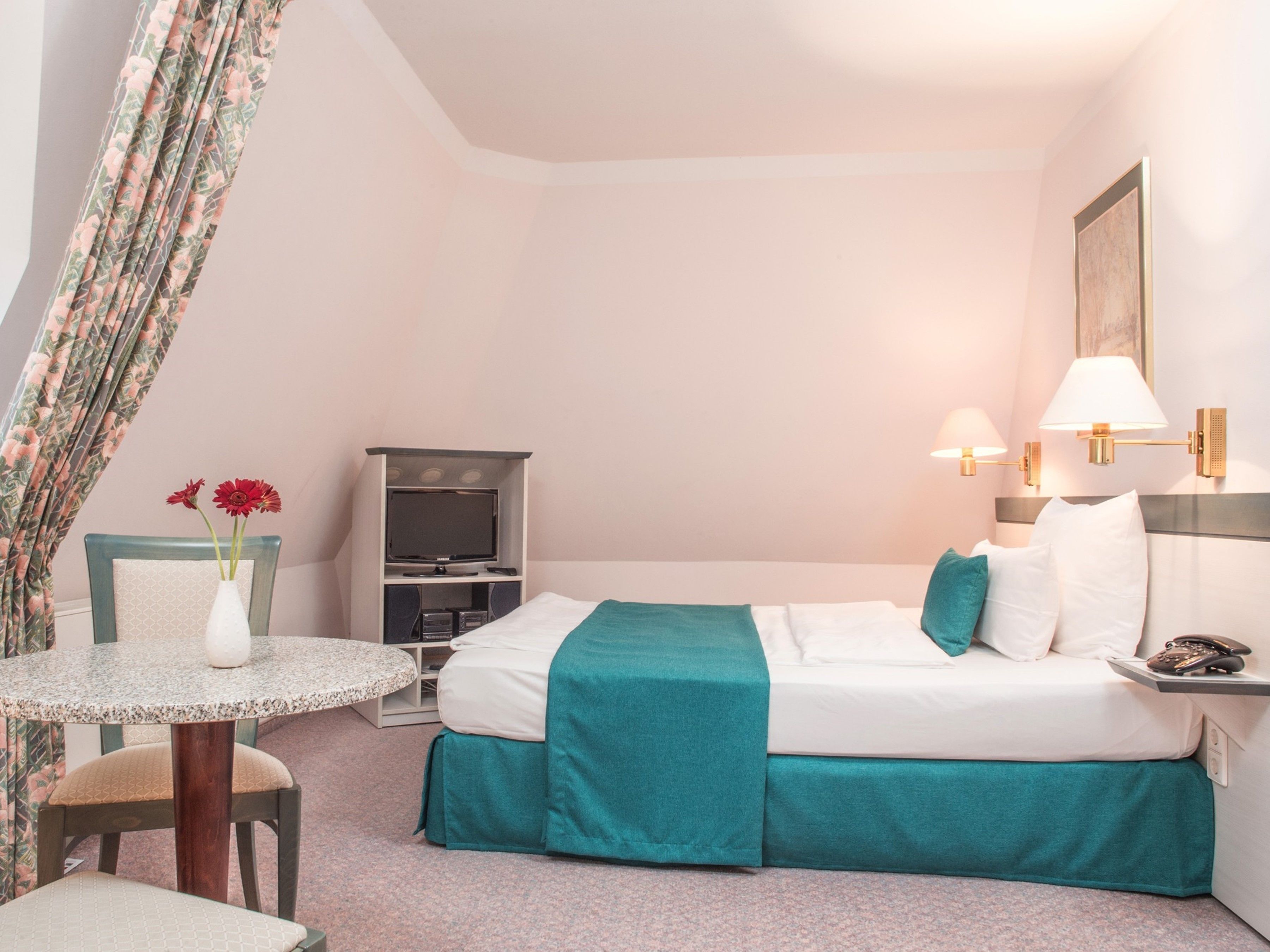 A hotel room with a bed, a TV, a table with a vase of flowers, and a chair.
