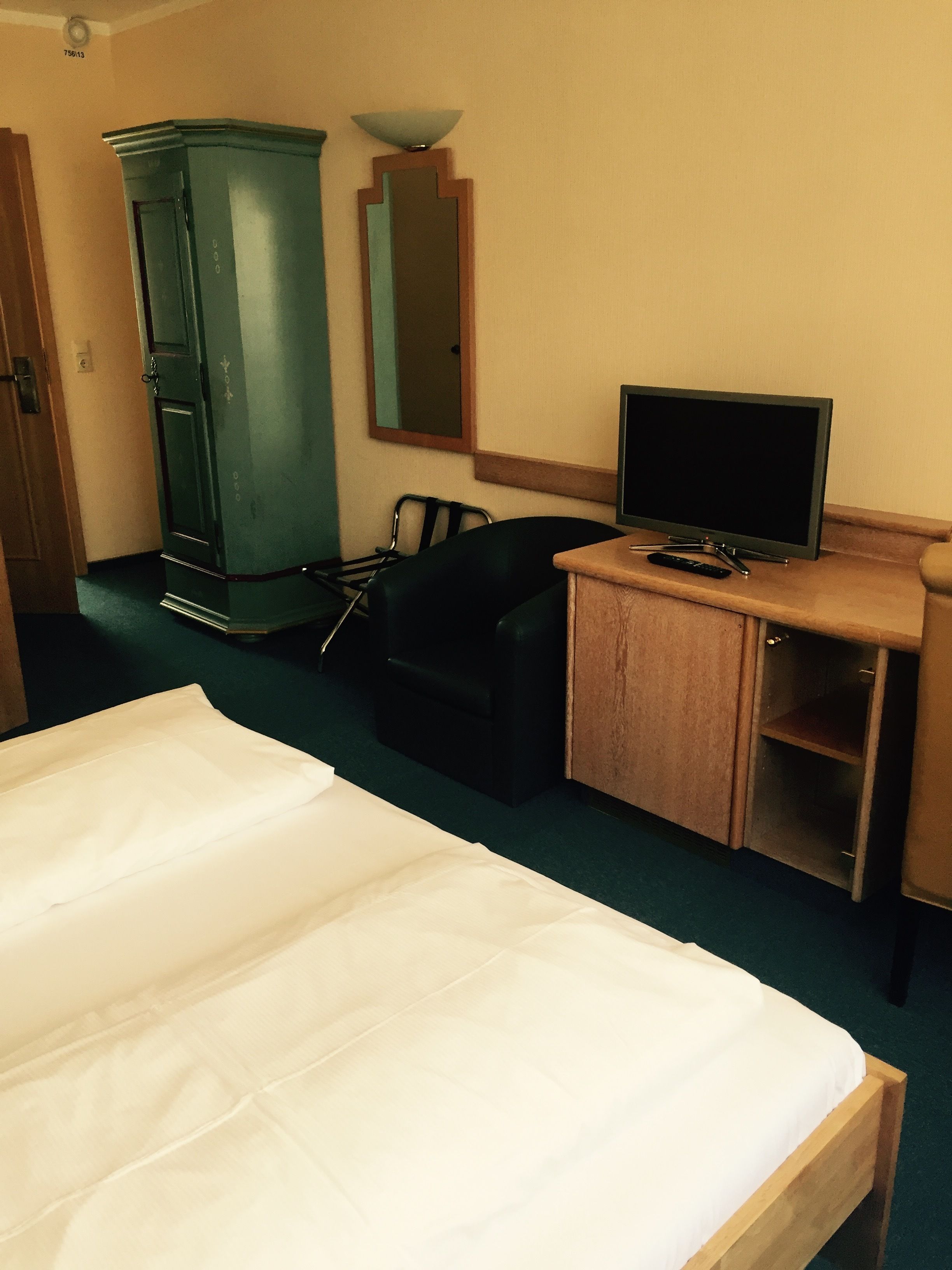 Een hotelkamer met een bed, een bureau met een televisie, een stoel, een kledingkast en een spiegel.