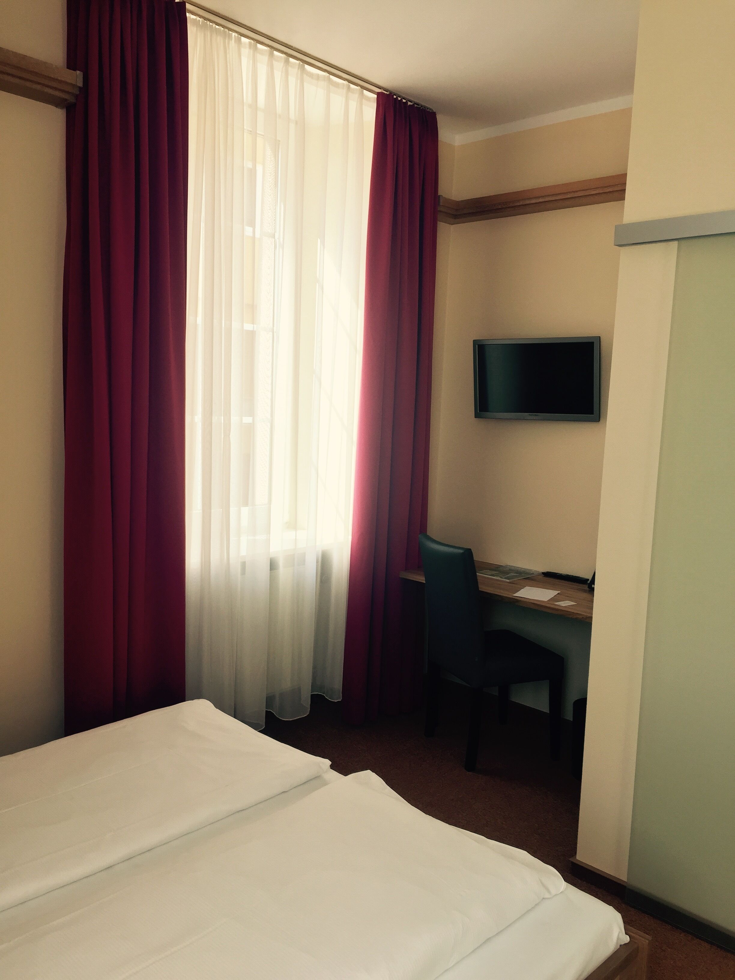 Quarto de hotel com cama, escrivaninha e televisão.