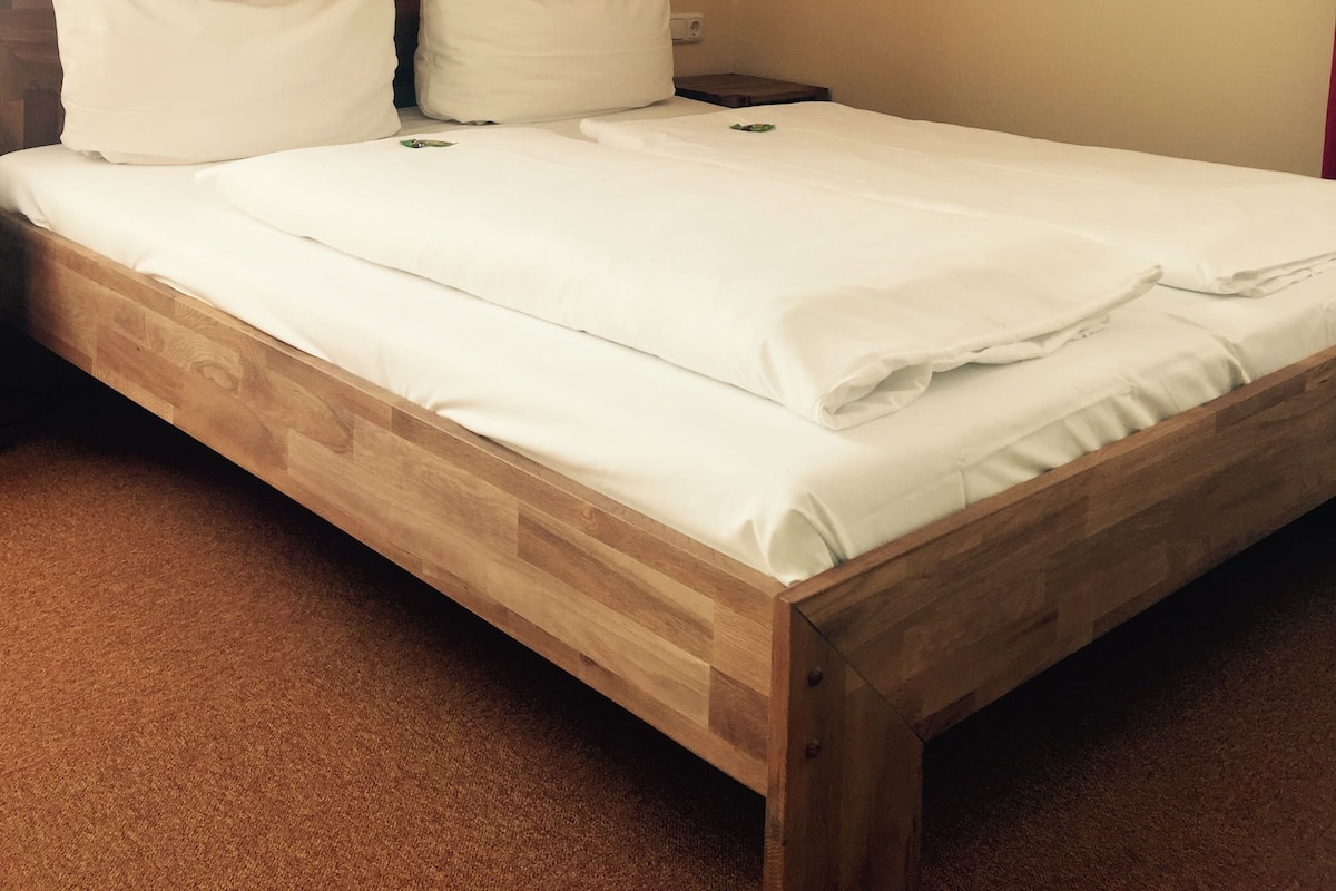 A hotel room with a wooden bed, white bedding, a painting of flowers on the wall, and a round wall clock.