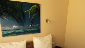 Hotelkamer met een bed, witte lakens, een schilderij van een strand en een nachtkastje met een lamp.