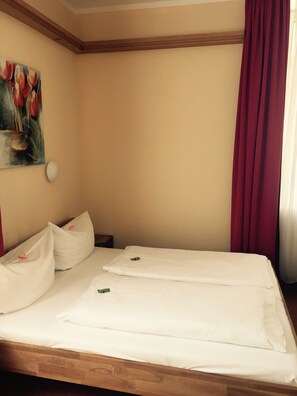 A hotel room with a wooden bed frame, white bedding, a painting of flowers on the wall, and a red curtain. - Hotel Gerber (Hoesbach)