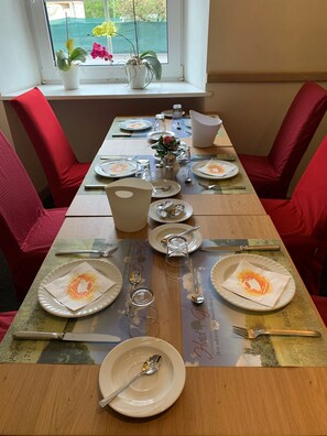 A dining table set with plates, cutlery, and glasses, surrounded by red upholstered chairs. - Hotel Gerber (Hoesbach)