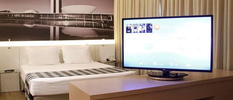 Una habitación de hotel con una cama, un televisor sobre un soporte de madera y un cuadro colgado en la pared.