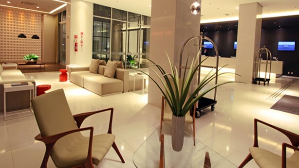 Un hall d’hôtel moderne comprenant un espace salon, un comptoir d’accueil et une grande plante en pot.
