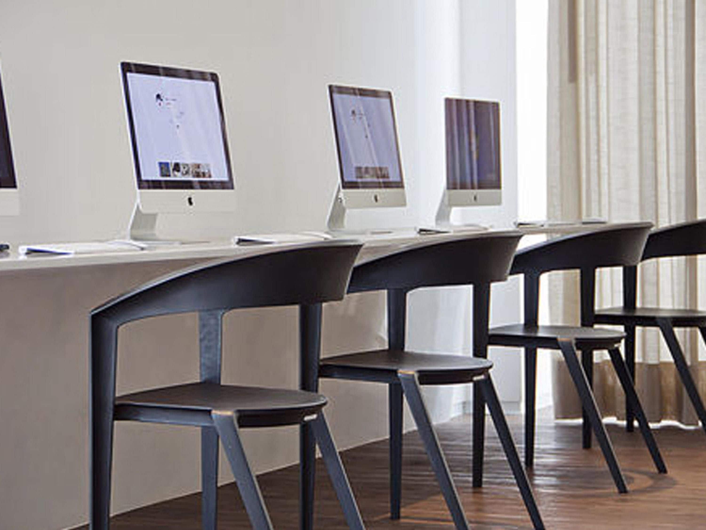 Une rangée d’écrans d’ordinateur sur un bureau blanc, avec des chaises noires.