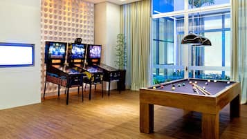 Una habitación moderna con mesa de billar, tres máquinas de videojuegos y un ventanal con cortinas.