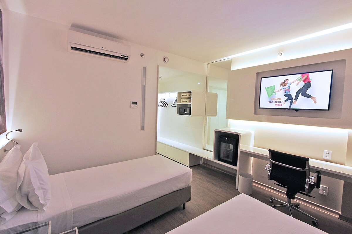 Een hotelkamer met een bed, bureau, stoel, televisie en spiegel.