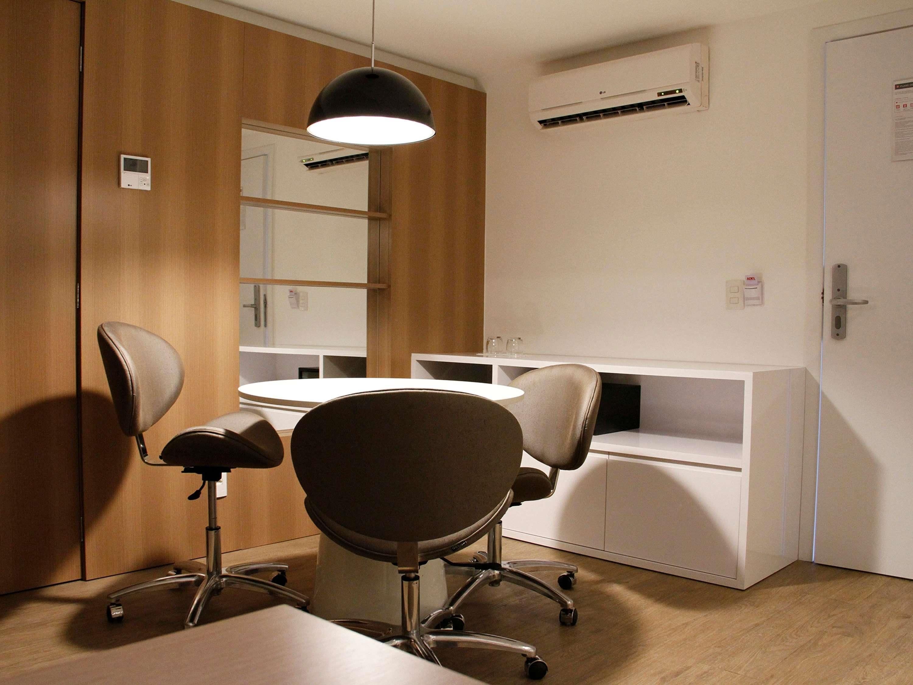 A conference room with a round table, two office chairs, a pendant light, a whiteboard, and a whiteboard stand.