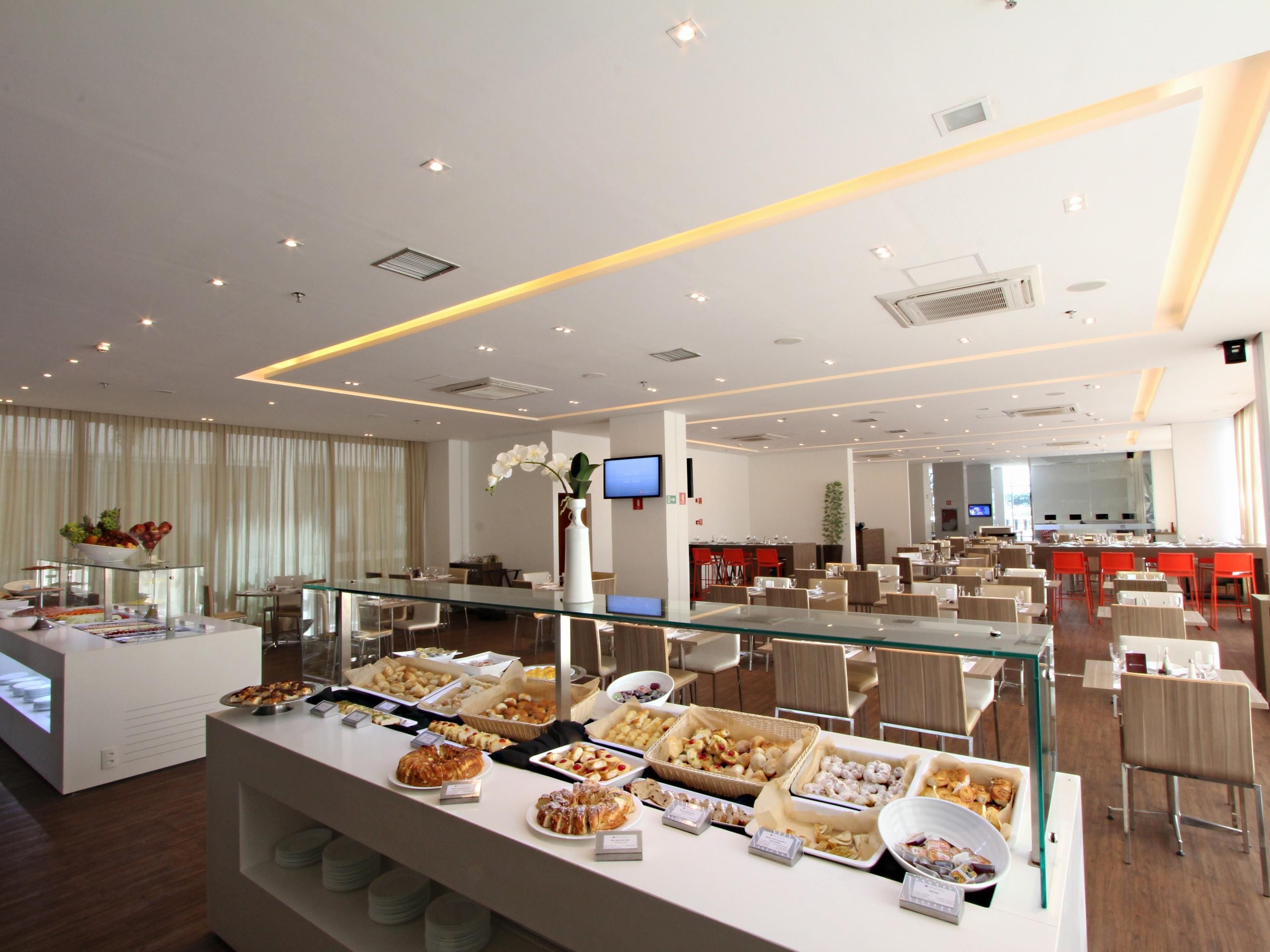 Zona de bufé con diferentes opciones de comida, un expositor de vidrio y un área de comedor con mesas y sillas.