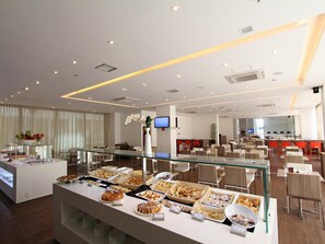 Ein Bereich mit Buffet, verschiedenen Speisen, einer Glasvitrine und einer Sitzgelegenheit mit Tischen und Stühlen.