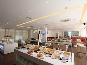 Un espace buffet proposant divers plats, une vitrine réfrigérée et un coin salon avec des tables et des chaises.