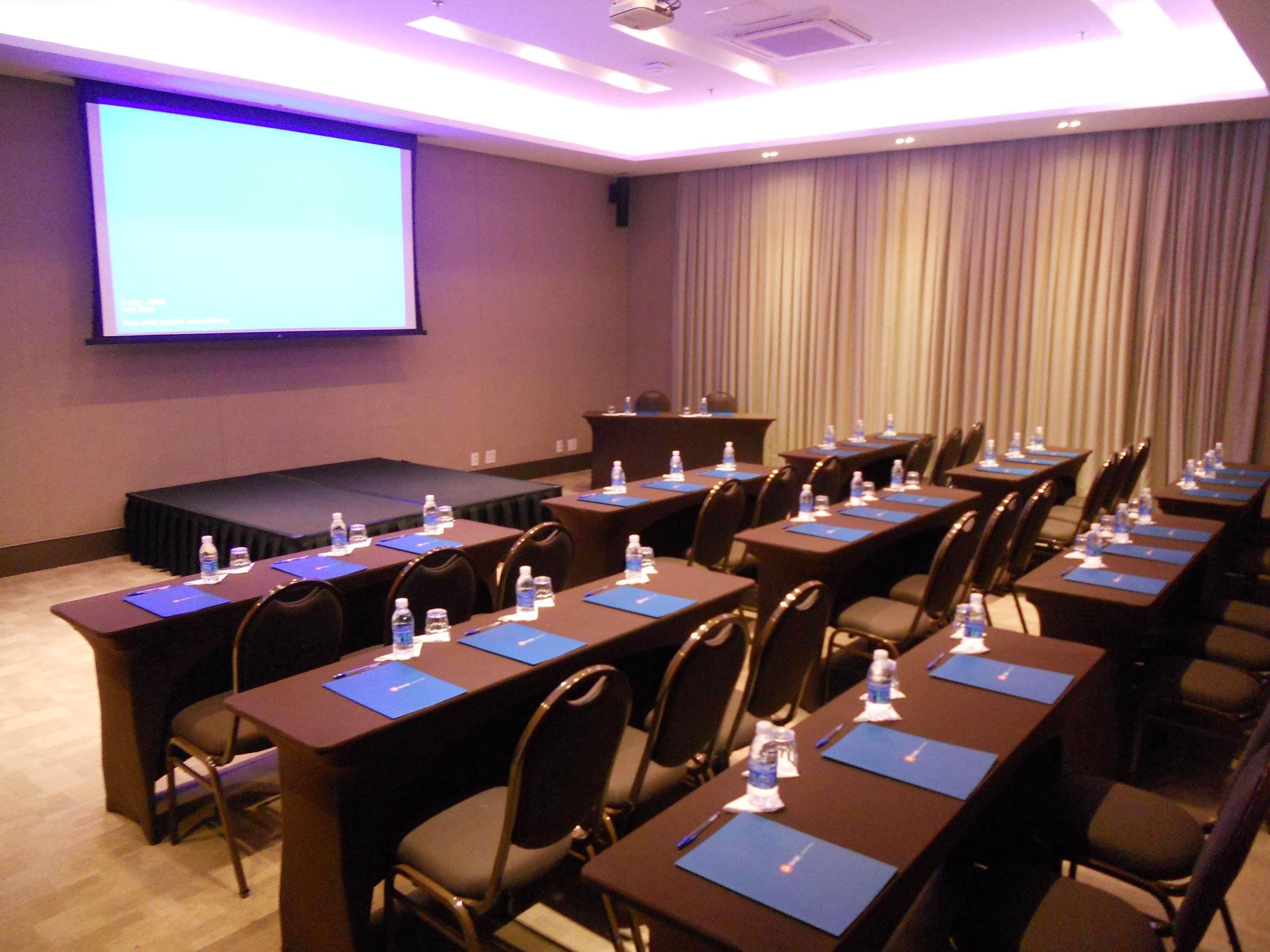 A conference room with rows of tables, chairs, and a projector screen.