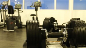 Een sportschool met trainingsapparatuur, waaronder gewichten en loopbanden, en grote ramen op de achtergrond.