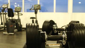 A gym with exercise equipment, including dumbbells and treadmills, and large windows in the background.