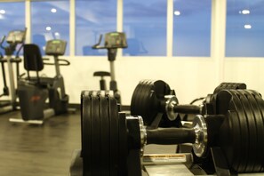 Een sportschool met trainingsapparatuur, waaronder gewichten en loopbanden, en grote ramen op de achtergrond.