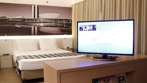 Une chambre d’hôtel avec un lit, un téléviseur posé sur un meuble en bois et un tableau accroché au mur.