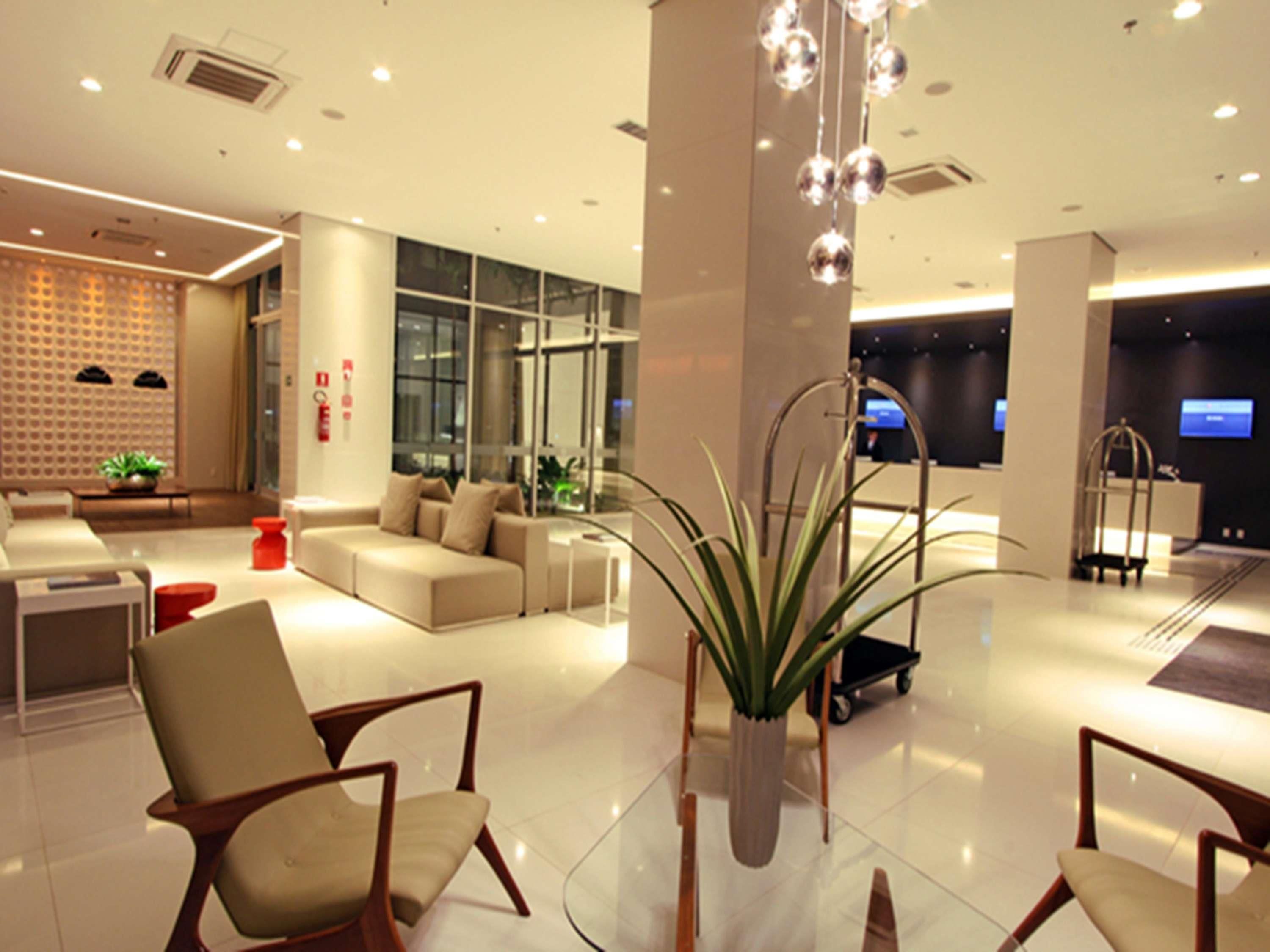Un moderno vestíbulo de hotel con zona de estar, mostrador de recepción y una gran planta en maceta.
