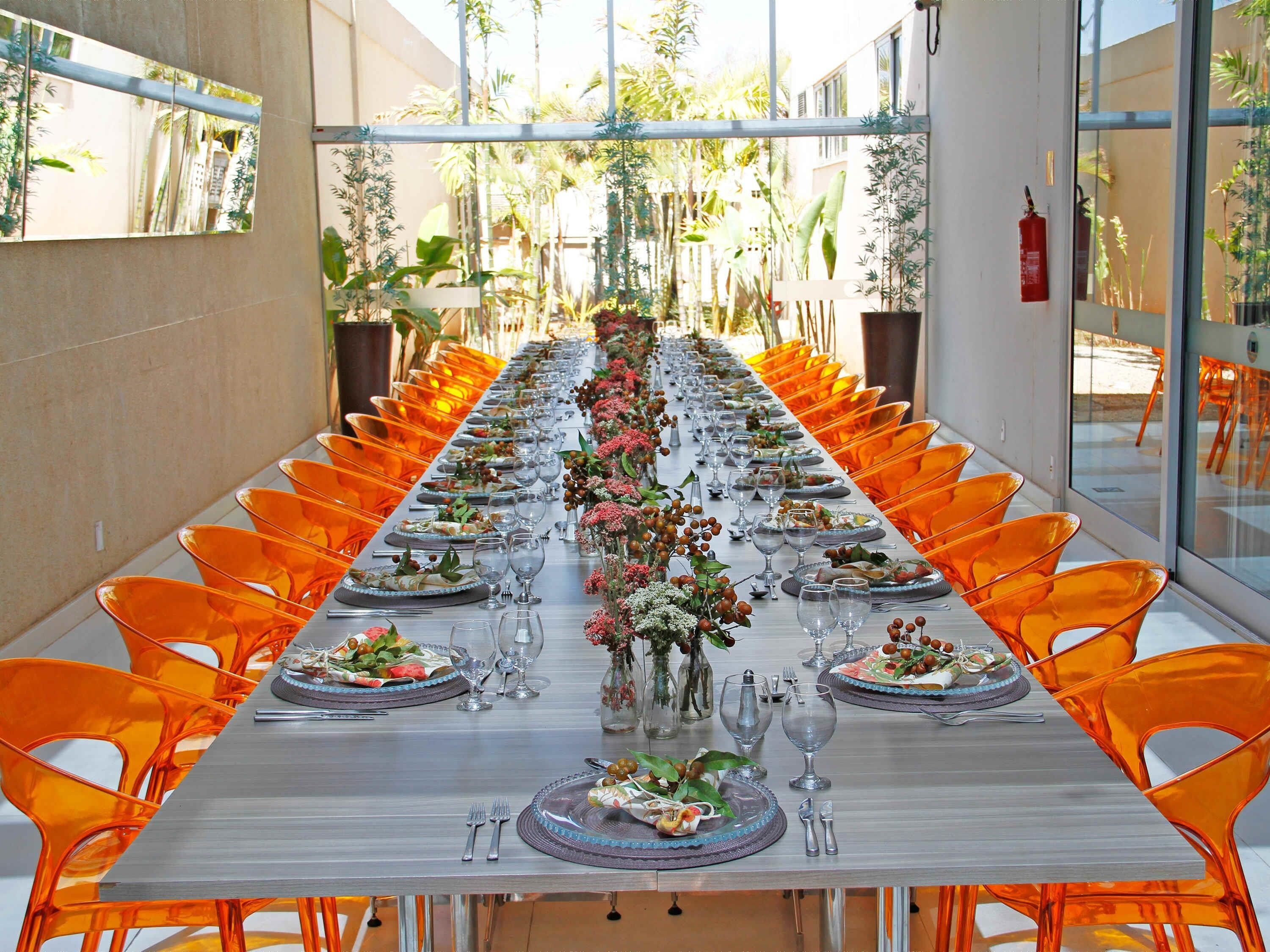 A long dining table with orange chairs, set with plates, glasses, and cutlery.