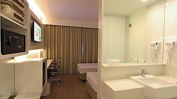 Quarto de hotel com escrivaninha, cadeira, cama e banheiro com pia e espelho.
