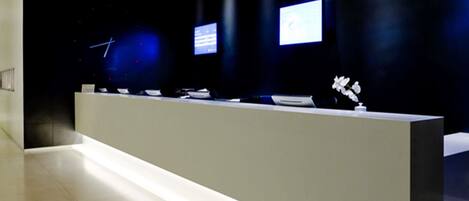 A modern reception desk with a flat surface, a small desk lamp, and a vase with flowers.