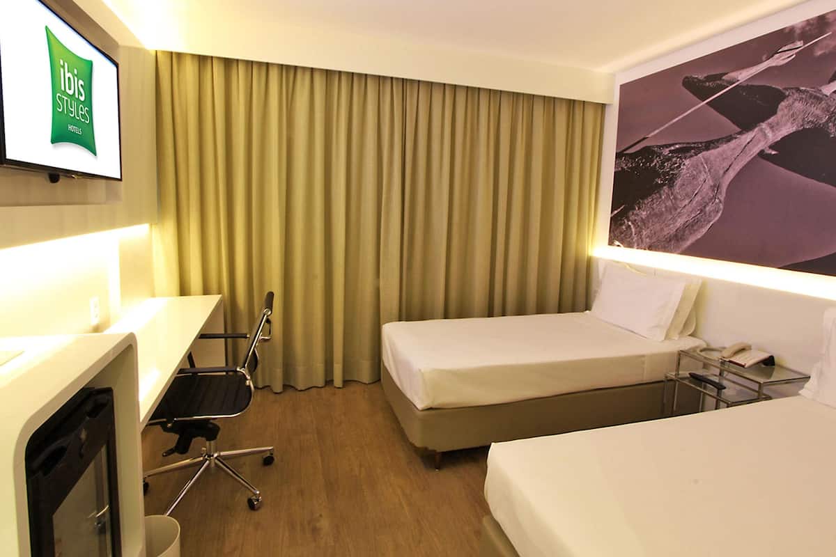 Una habitación de hotel con una cama, un escritorio, una silla, un televisor y una cortina.