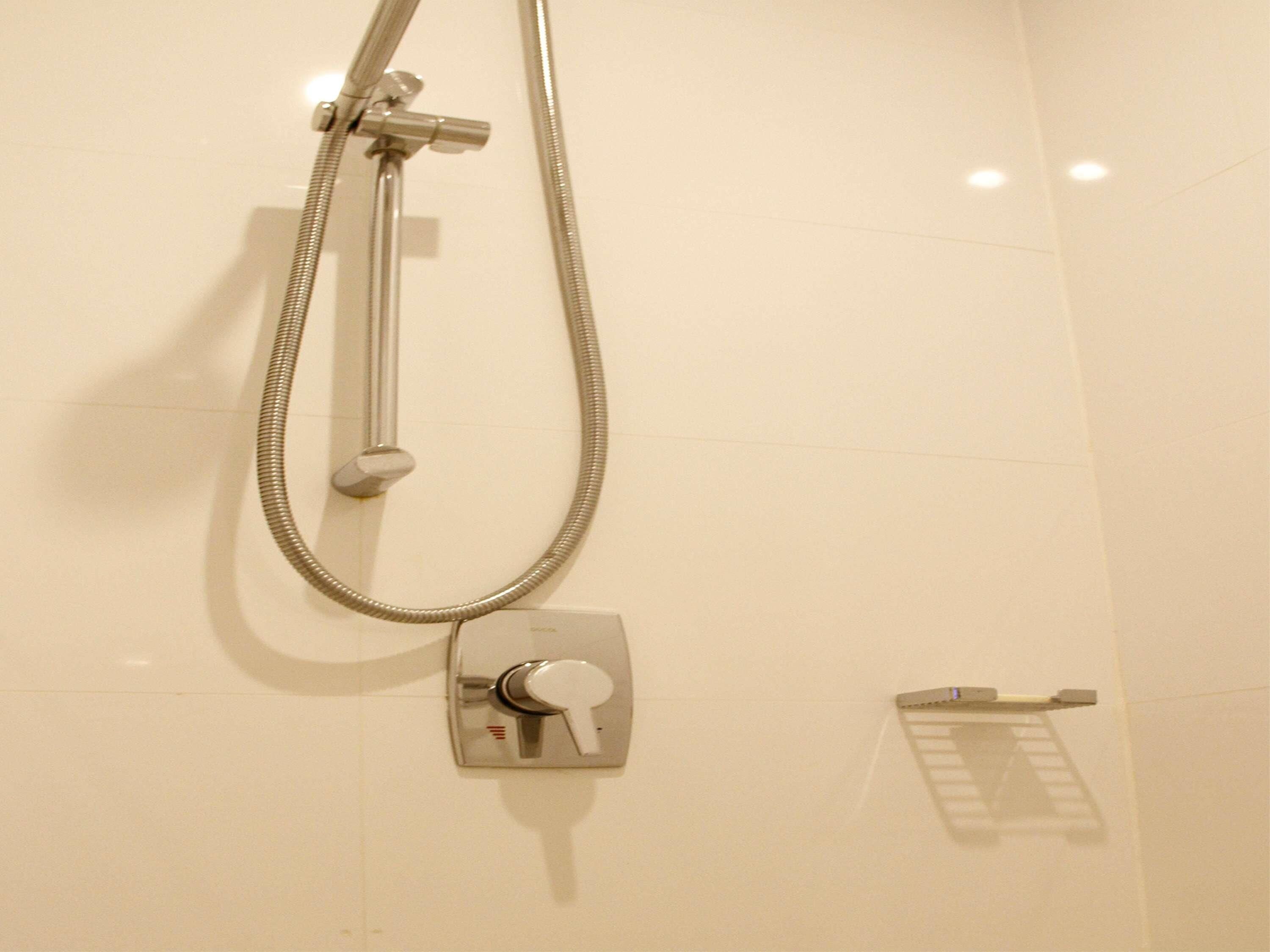 Une douche équipée d’un pommeau de douche à main et d’un panneau de commande fixé au mur.
