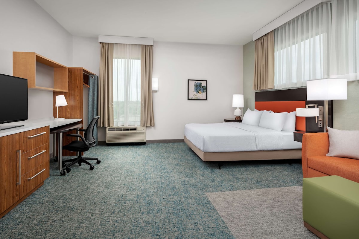 Una habitación de hotel con cama, escritorio con computadora, televisor y armario.