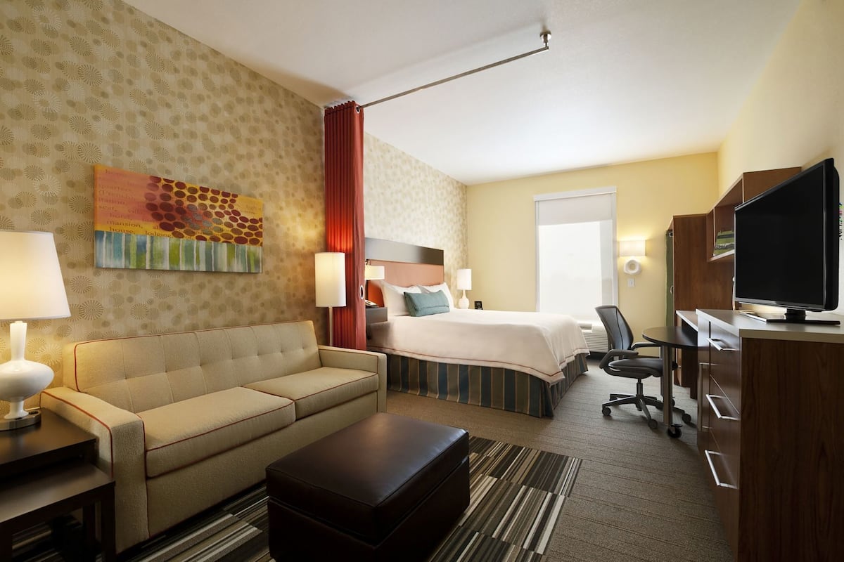 Una habitación de hotel con sofá, cama, escritorio, televisión y ventana.