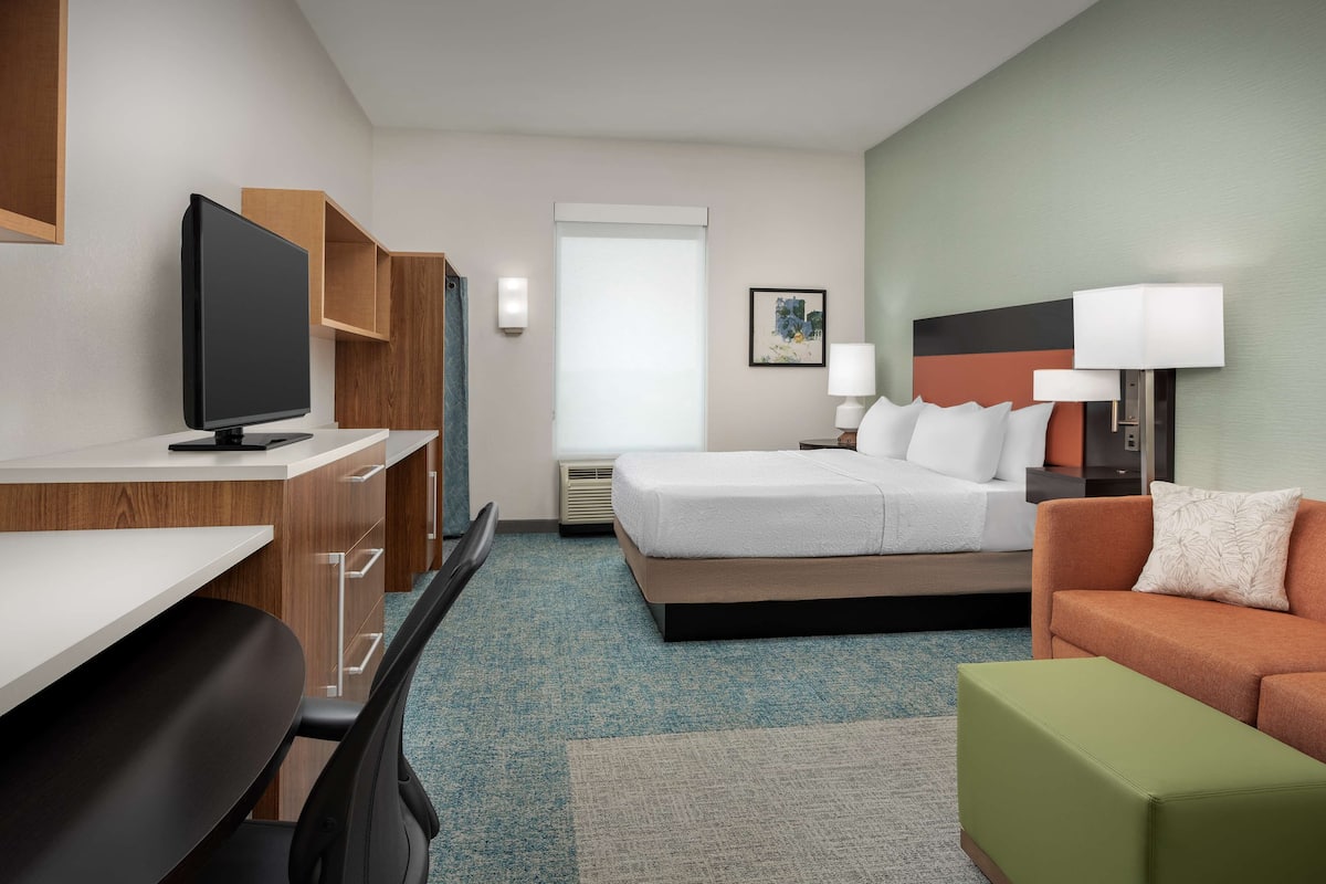 Una habitación de hotel con cama, escritorio con computadora, sofá y televisión.