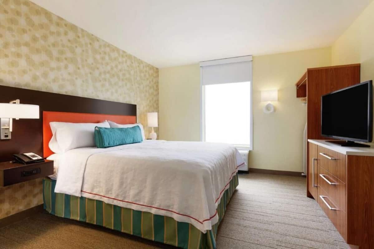 Una habitación de hotel con cama, televisión, mesita de noche y ventana.