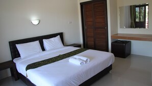 A neatly made bed with white linens and a rolled towel, a dark wooden headboard, a small bedside table, a dark ottoman, a wall-mounted light, and a mirror reflecting a window with curtains. - Kanlaya Park Apartment Hotel (Koh Samui)