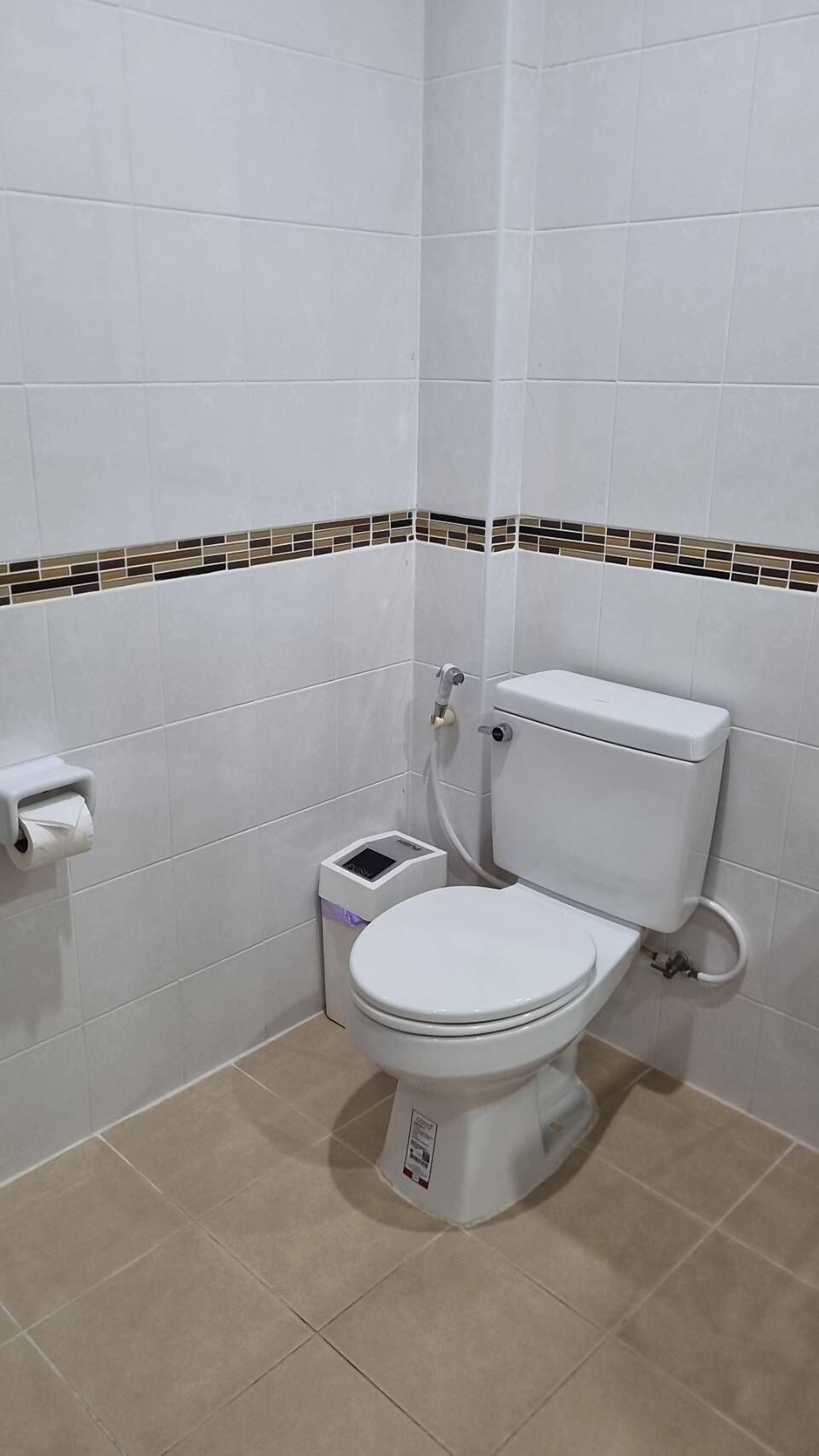 Un inodoro pequeño y blanco con tanque, un bidé y un dispensador de papel higiénico en la pared.