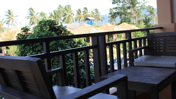A wooden deck with a table and chairs, overlooking a view of palm trees and buildings. - Kanlaya Park Apartment Hotel (Koh Samui)