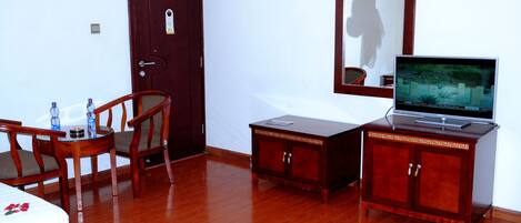 A hotel room with a wooden bed, a small table with chairs, a wooden cabinet with a television, and a door.