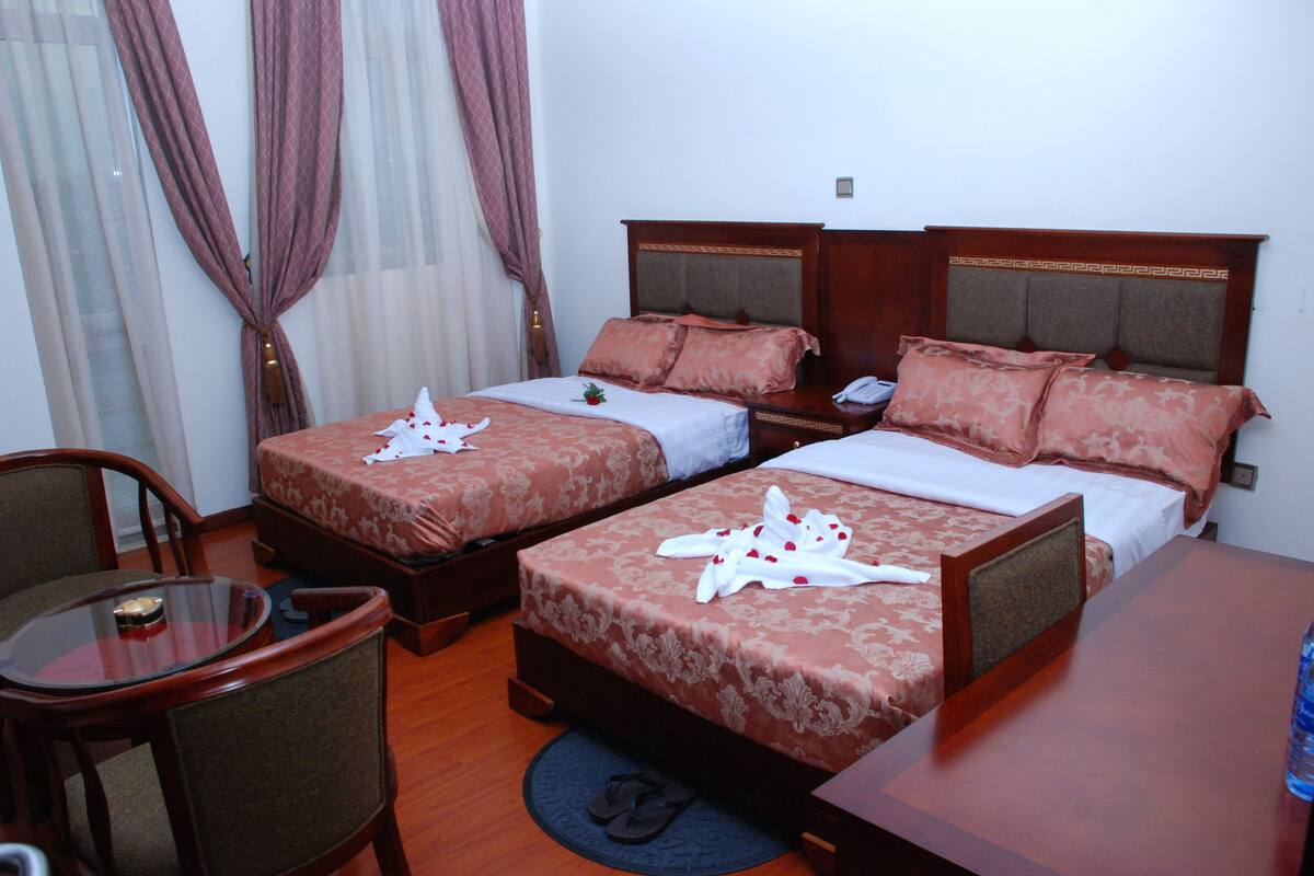 A hotel room with two beds, a wooden table, and a chair.