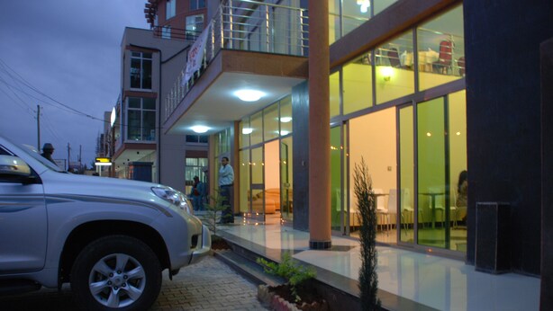 A modern building with a glass facade, a paved entrance, and a parked car. - Addis Amba Hotel (Bahir Dar)