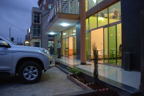 Un edificio moderno con fachada de vidrio, entrada pavimentada y un automóvil estacionado.