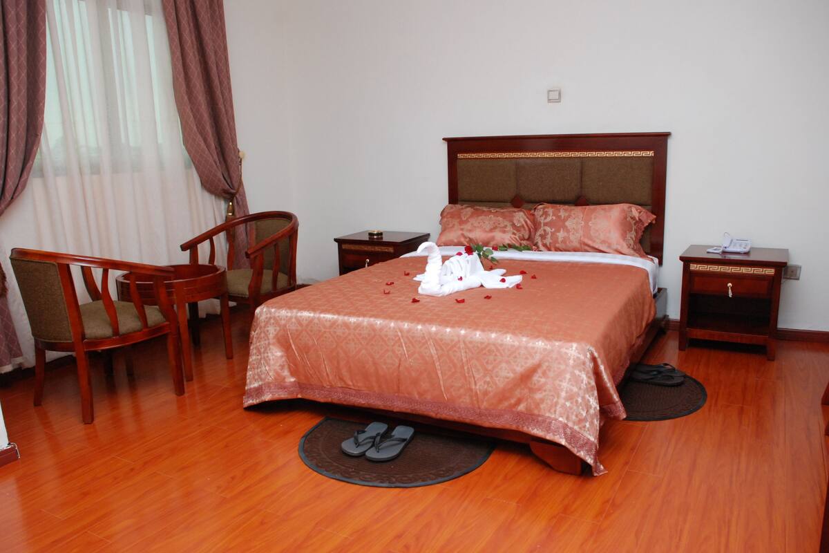 A neatly arranged hotel room with a large bed, a chair, a nightstand, and a bedside table.